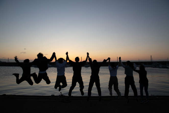 夕暮れの海に向かってジャンプする若者たち