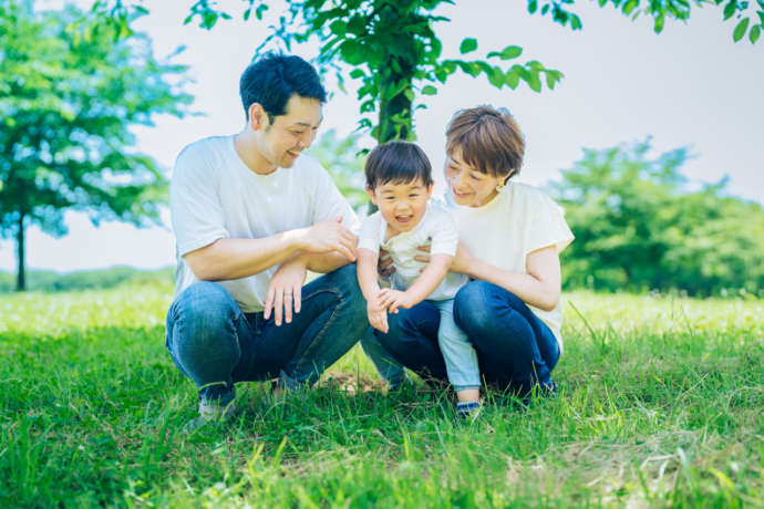 晴天の緑地に座る親子3人