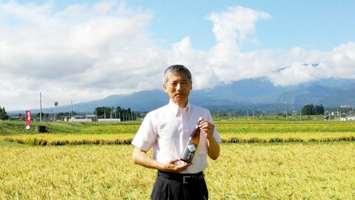 圃場で日本酒を持って立つ杜氏の早津さん