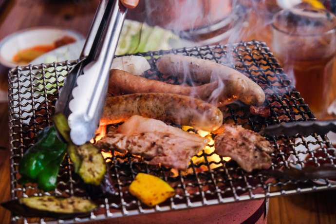 焼き肉用のモンヴェールポークやソーセージ、野菜を炭火で焼く様子