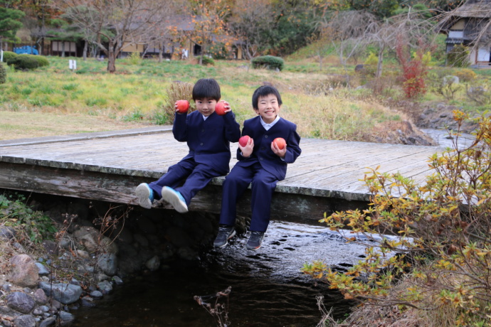 ふたりの子どもがりんごを持って小さな橋に腰かけている写真