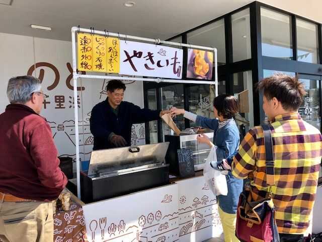 道の駅「のと千里浜」の軒下で焼き芋を販売する人と客3人