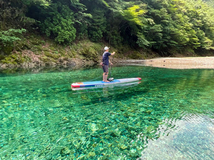 RocaRocaアクティビティがある宮川の透き通る水とSUPをする男性