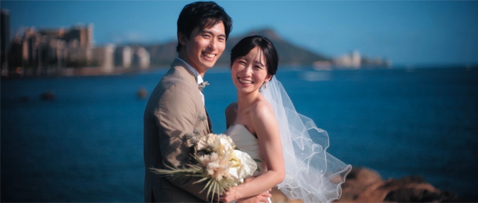 ハワイのキラキラ光るビーチを手をつないで歩く新郎新婦