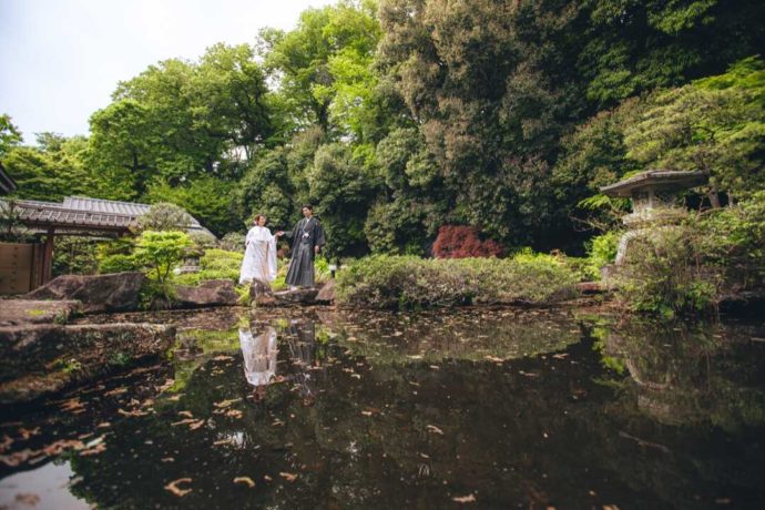 庭園の池の縁を手を取り合って歩く和装姿の新郎新婦