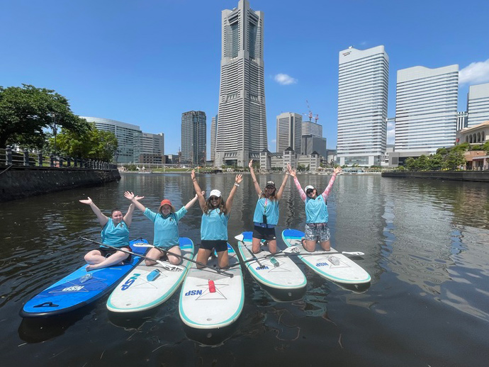 水辺荘のSUP体験ツアーに参加中の外国人の皆さん（みなとみらい地区を背景に）