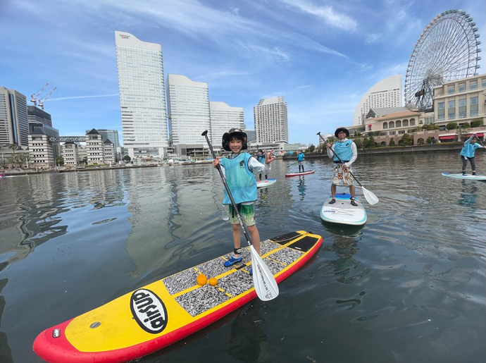 水辺荘のSUP体験ツアーに参加中の皆さん（みなとみらい地区を背景に）