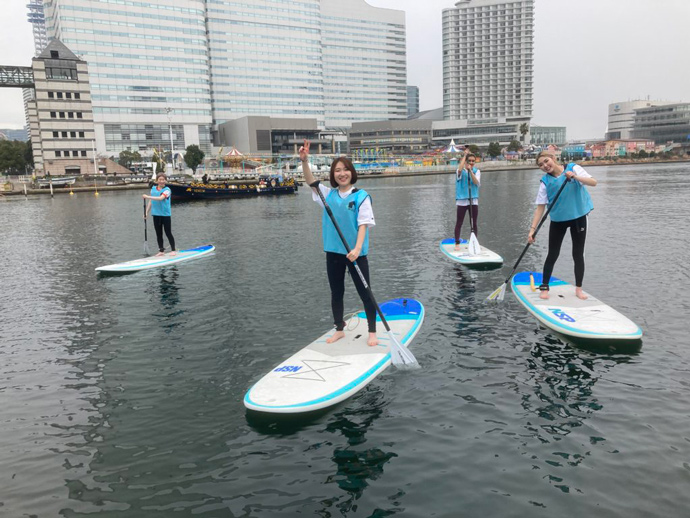 水辺荘のSUP体験ツアーに参加中の皆さん（みなとみらい地区を背景に）