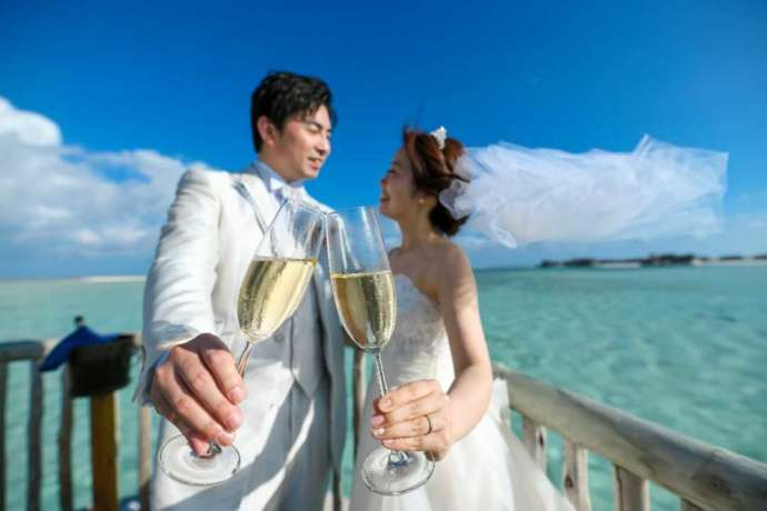 モルディブの美しい海を背景にシャンパンで乾杯する新郎新婦