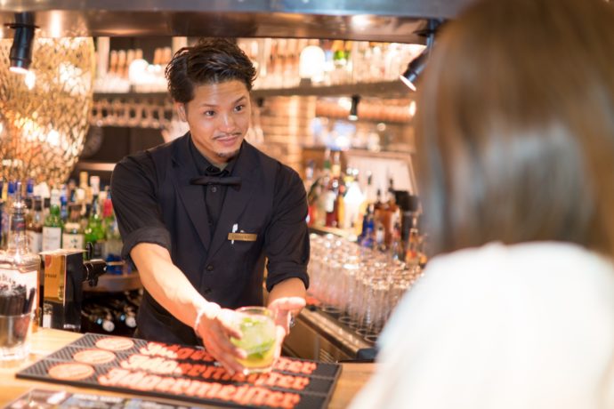 バーでお酒を提供するPUBLIC STANDパブスタのスタッフと女性客