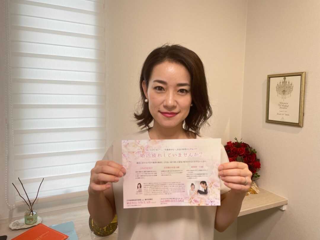 婚活サロンSWEARのチラシを持って微笑む代表カウンセラーの吉本さん