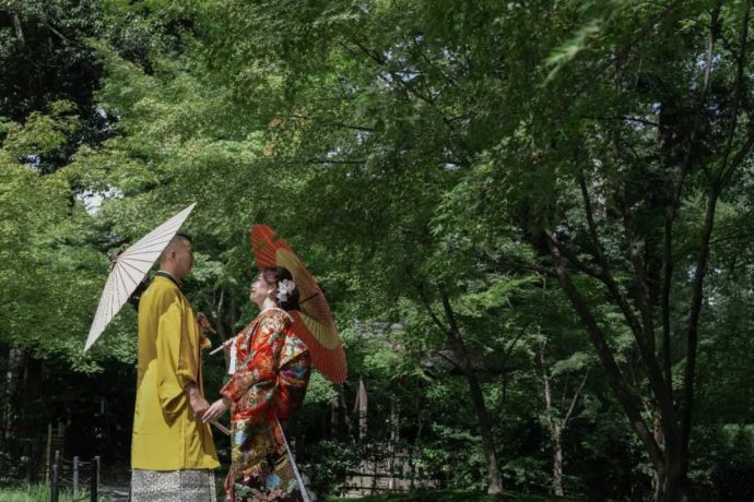 緑溢れる庭園内で番傘をさし見つめ合う和装の新郎新婦