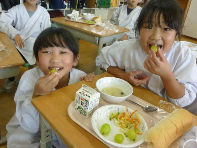 給食のぶどうを食べる笑顔の子ども